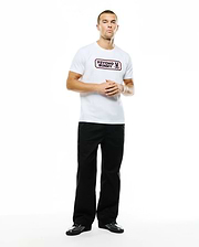 Men's Samson Wordmark Graphic Tee, a white classic fit jersey t-shirt featuring a prominent pink Psycho Bunny wordmark and skull logo graphic on the chest, paired with relaxed black wide-leg pants. (5)