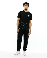 Mens Malcolm Graphic Tee. Black classic fit jersey tee with white and teal paint splatter graphic on the lower front and a small white Psycho Bunny text logo on the left chest.
