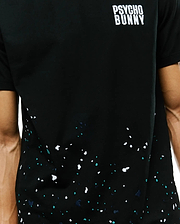 Mens Malcolm Graphic Tee, classic fit black jersey t-shirt featuring a white Psycho Bunny text logo on the upper chest and a vibrant white, teal, and navy splatter graphic.