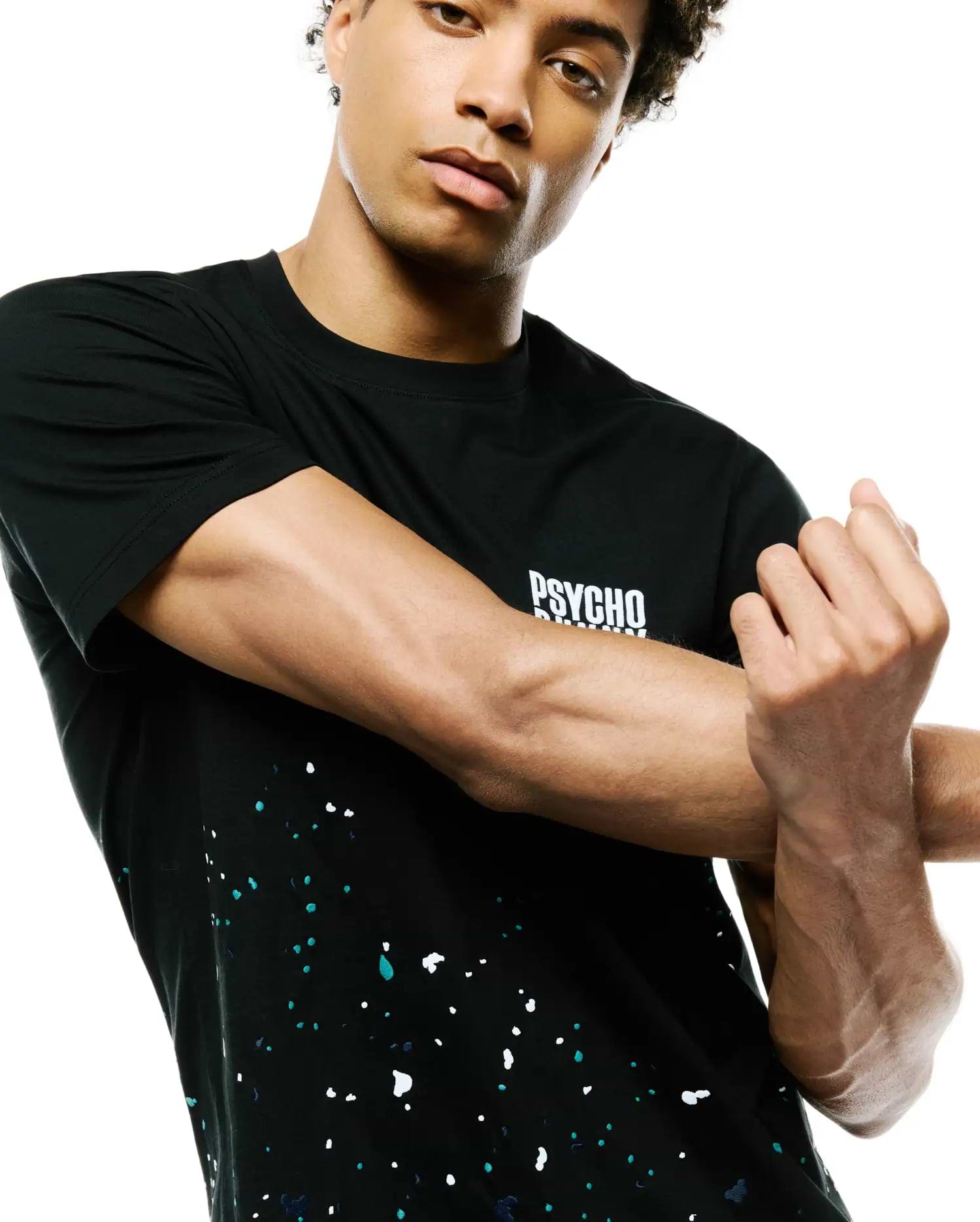 Mens Malcolm Graphic Tee, a black jersey knit t-shirt with a classic fit, featuring a white PSYCHO BUNNY text logo on the chest and a vibrant white, teal, and dark blue paint splatter graphic on the lower half.