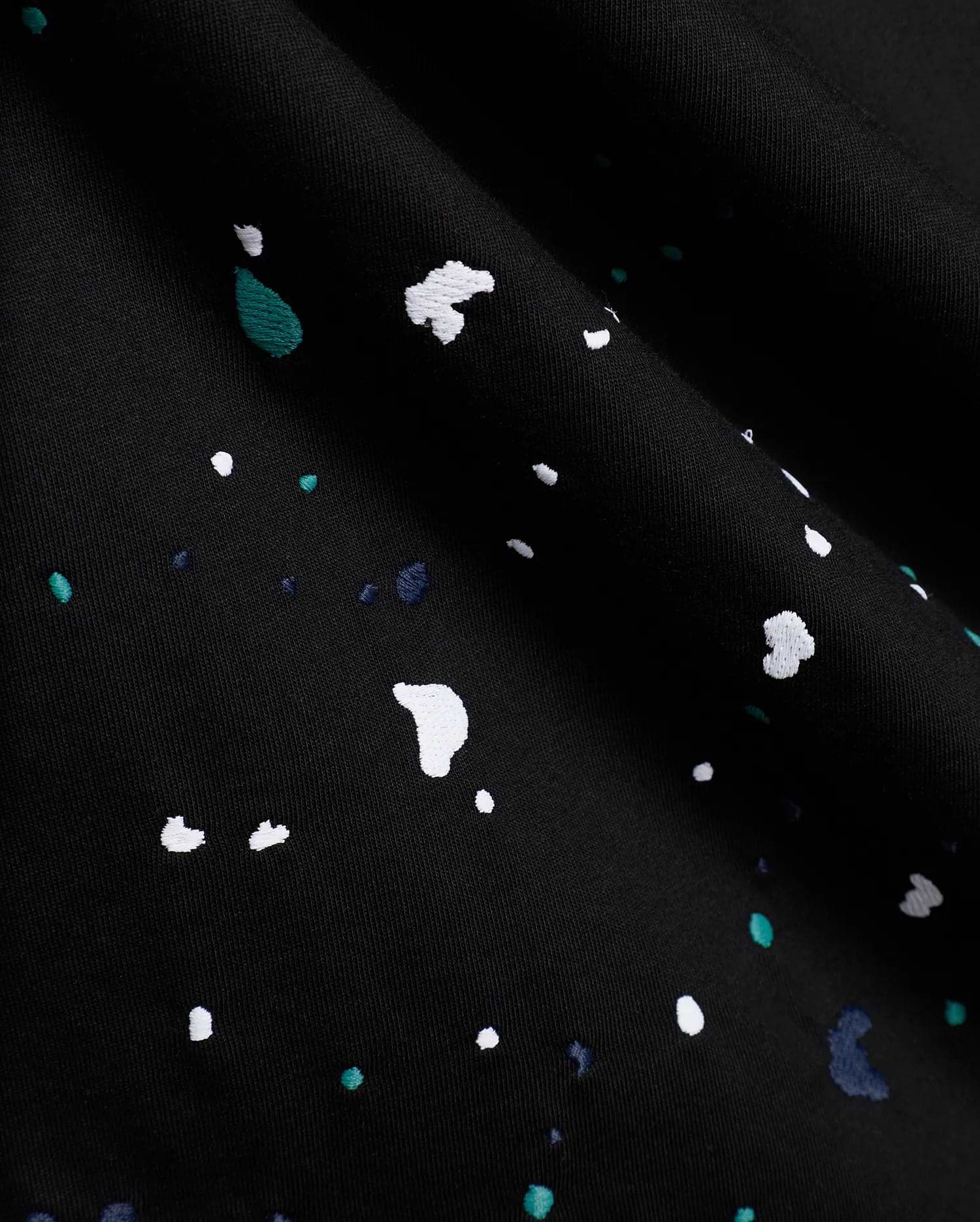 Black Mens Malcolm Graphic Tee crafted from smooth jersey knit fabric, adorned with an intricate embroidered paint splatter pattern in white, vibrant teal, and deep blue.