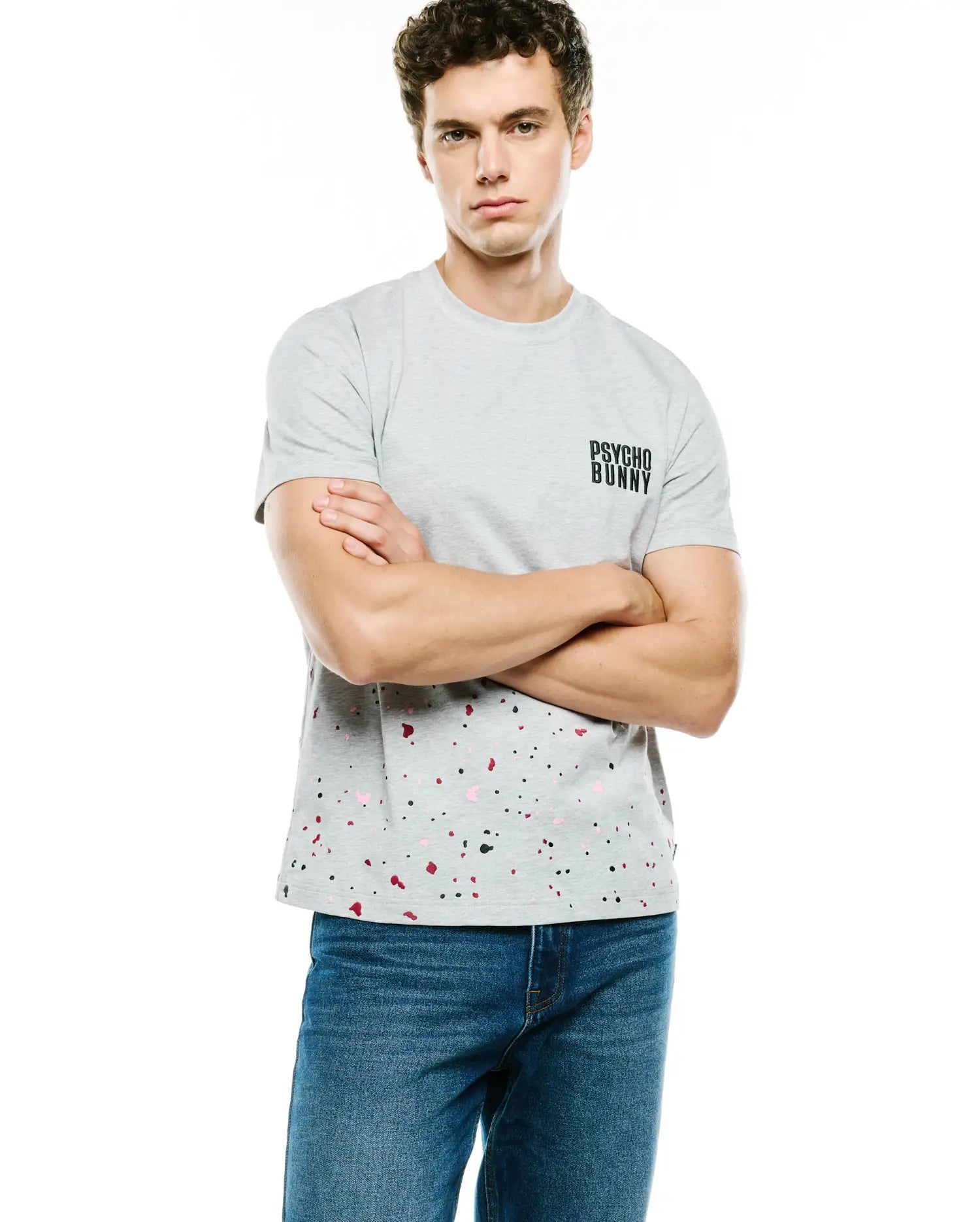 Mens Malcolm Graphic Tee, a grey classic fit jersey t-shirt featuring a small black Psycho Bunny text logo on the chest and a vibrant black, pink, and red paint splatter pattern on the lower half.