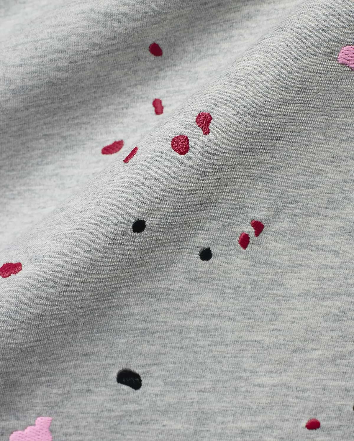Mens Malcolm Graphic Tee, a heather grey jersey knit fabric detailed with embroidered red, black, and pink paint splatter graphics for a bold, refined streetwear look.