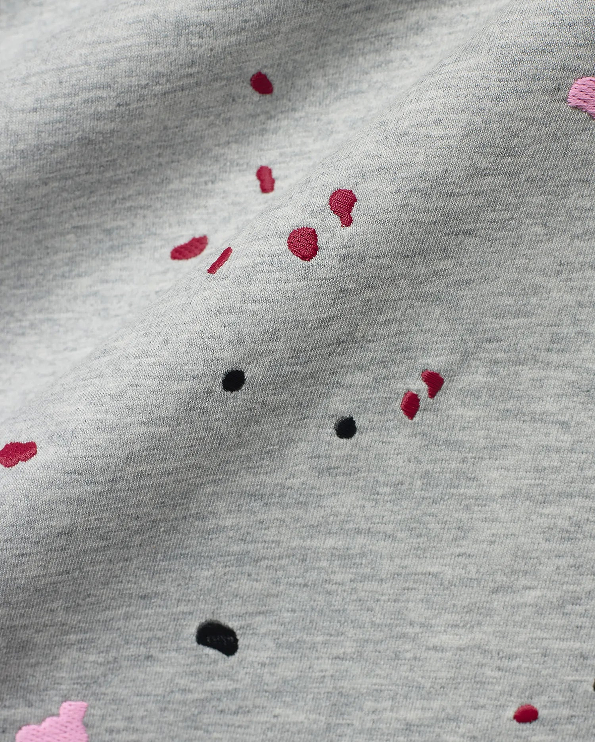 Mens Malcolm Graphic Tee, a heather grey jersey knit fabric detailed with embroidered red, black, and pink paint splatter graphics for a bold, refined streetwear look.