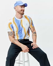Mens Blaze Sport Tee featuring a white base with a vibrant blue and orange wavy abstract print, classic fit, smooth jersey fabric, and a small embroidered Psycho Bunny skull logo on the left chest.