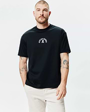 Mens Stevie Relaxed Fit Tee in black, featuring a small white Psycho Bunny skull and crossbones logo with arched text centered on the chest, made from smooth jersey knit fabric.