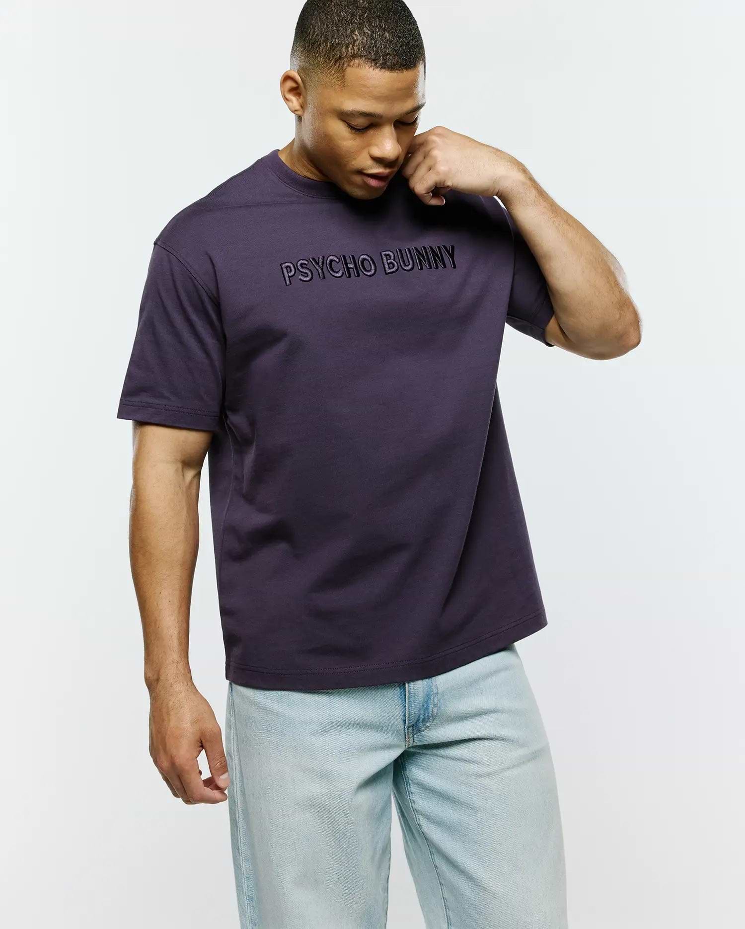 Dark purple Mens Windcrest Relaxed Fit Tee in smooth jersey knit, featuring a large, centered black embroidered PSYCHO BUNNY text logo on the chest.