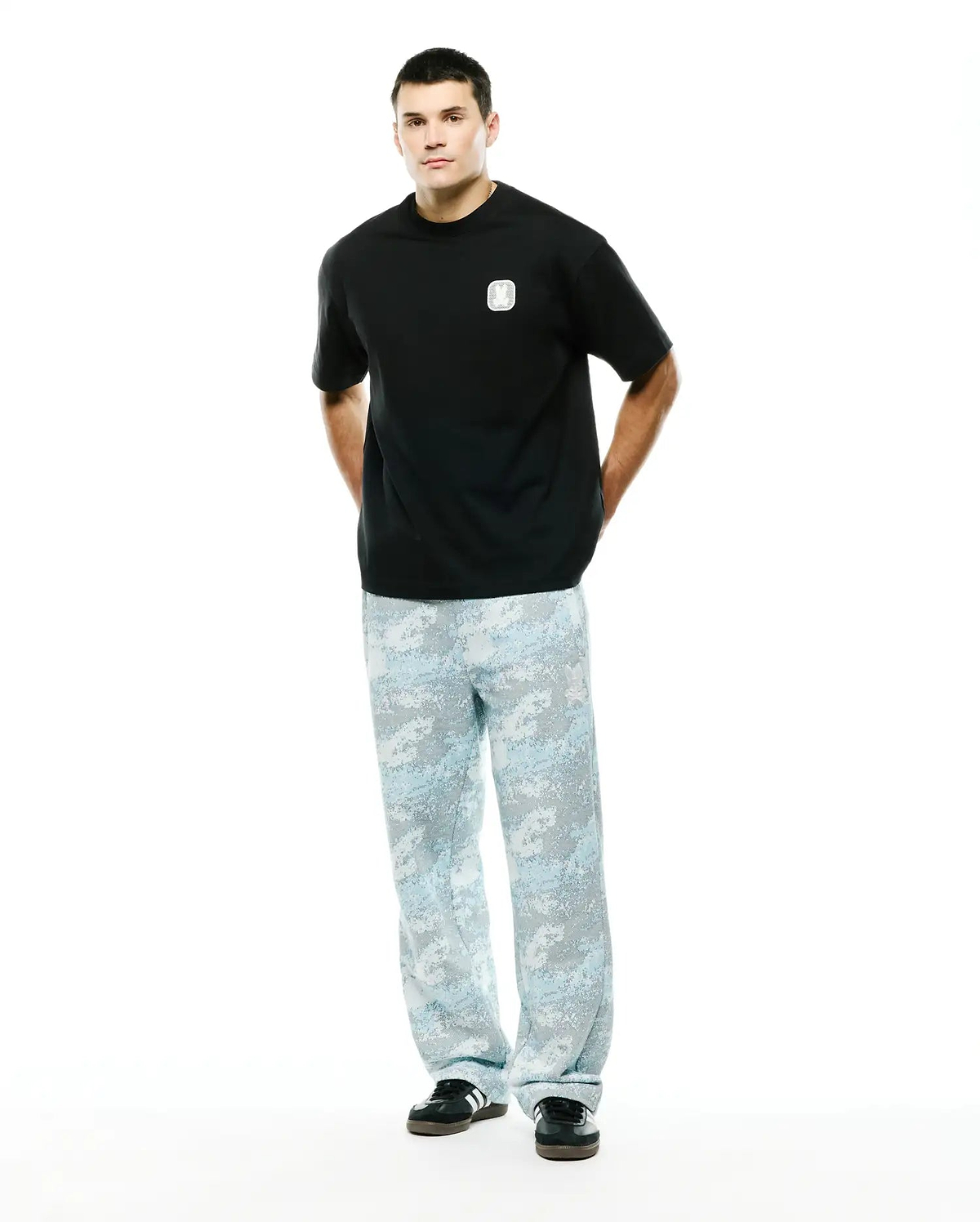 Men's Samson Oversized Bunny Tee in black jersey knit, featuring a small white embroidered Psycho Bunny skull logo on the left chest, paired with light blue and grey digital camouflage relaxed-fit pants. (4)