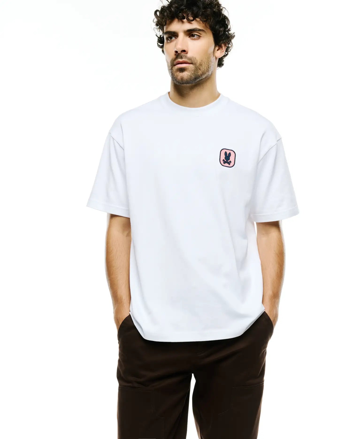 Men's Samson Oversized Bunny Tee, a white oversized jersey t-shirt featuring a small, embroidered Psycho Bunny skull logo with a pink checkered background on the left chest. (1)