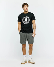 Mens Santa Fe Bunny Graphic Tee, a black classic fit premium jersey t-shirt featuring a large white circular Psycho Bunny skull logo graphic on the chest, complemented by grey textured knit drawstring shorts with a cuffed hem.