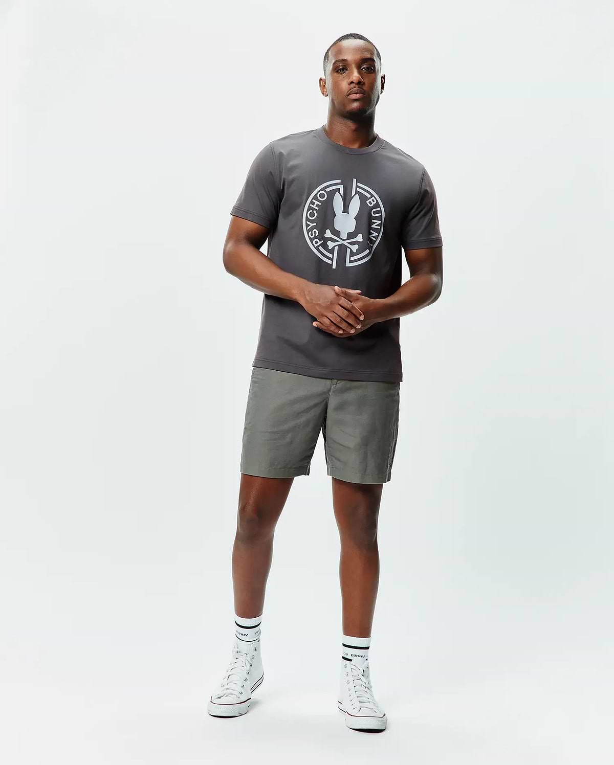 Mens Santa Fe Bunny Graphic Tee, a charcoal grey classic fit jersey t-shirt with a large white circular Psycho Bunny skull graphic on the chest, paired with olive green shorts. (4)