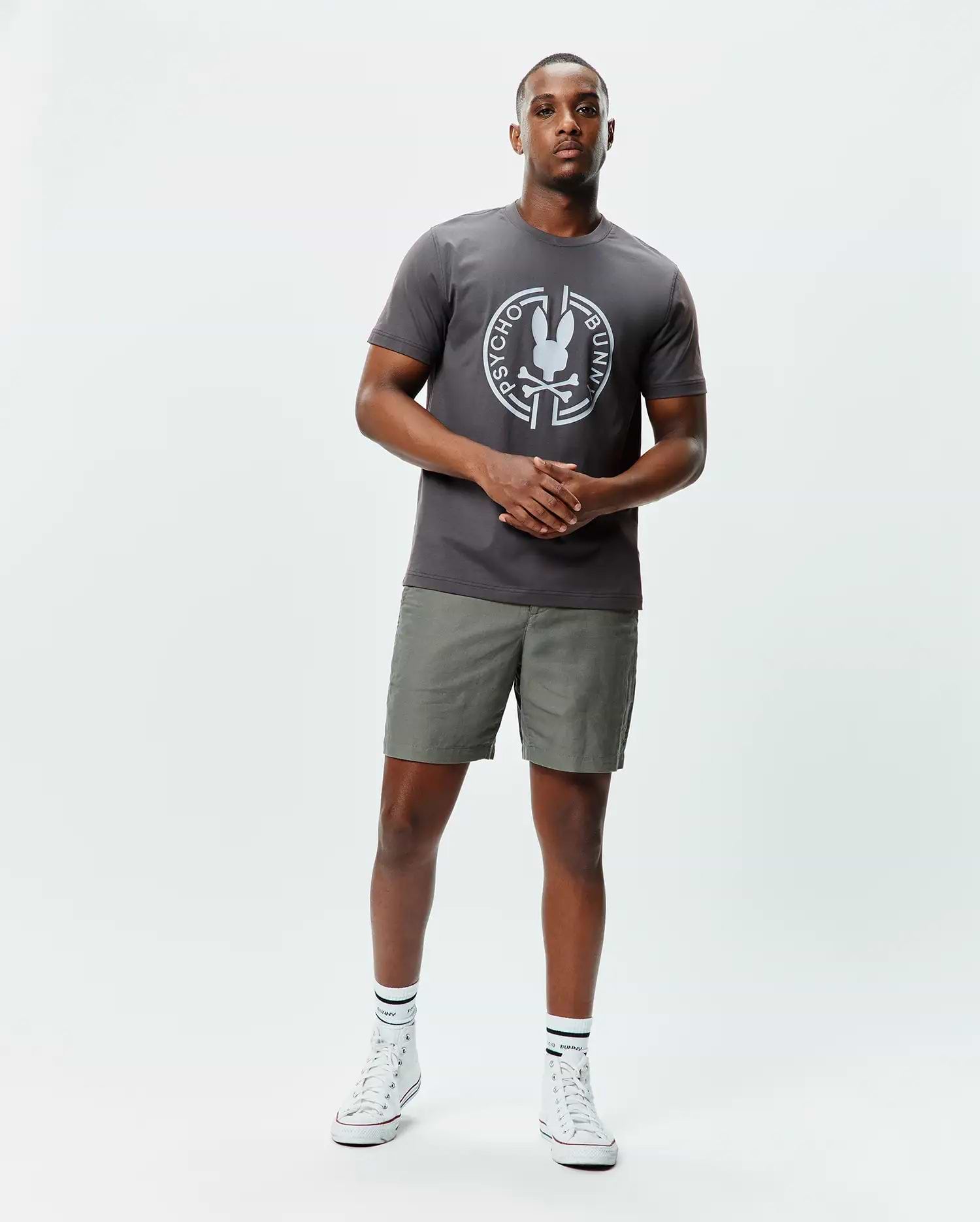Mens Santa Fe Bunny Graphic Tee, a charcoal grey classic fit jersey t-shirt with a large white circular Psycho Bunny skull graphic on the chest, paired with olive green shorts. (4)