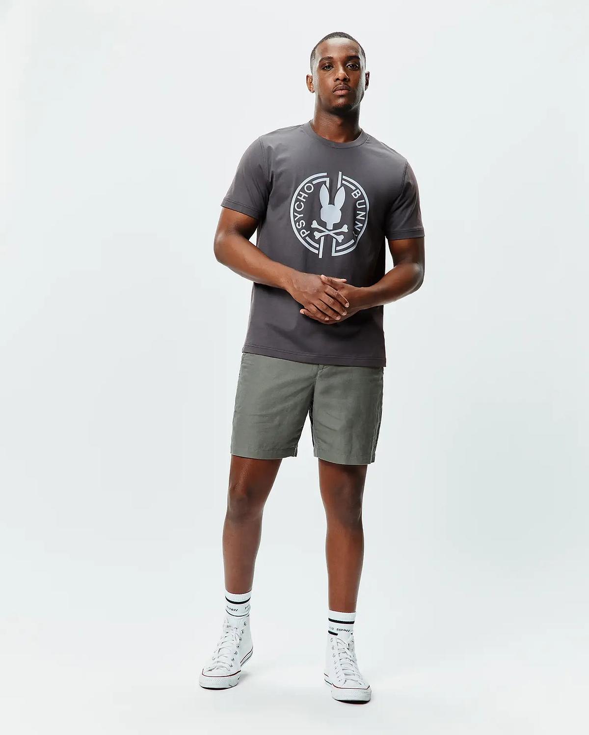 Mens Santa Fe Bunny Graphic Tee, a charcoal grey classic fit jersey t-shirt with a large white circular Psycho Bunny skull graphic on the chest, paired with olive green shorts. (4)