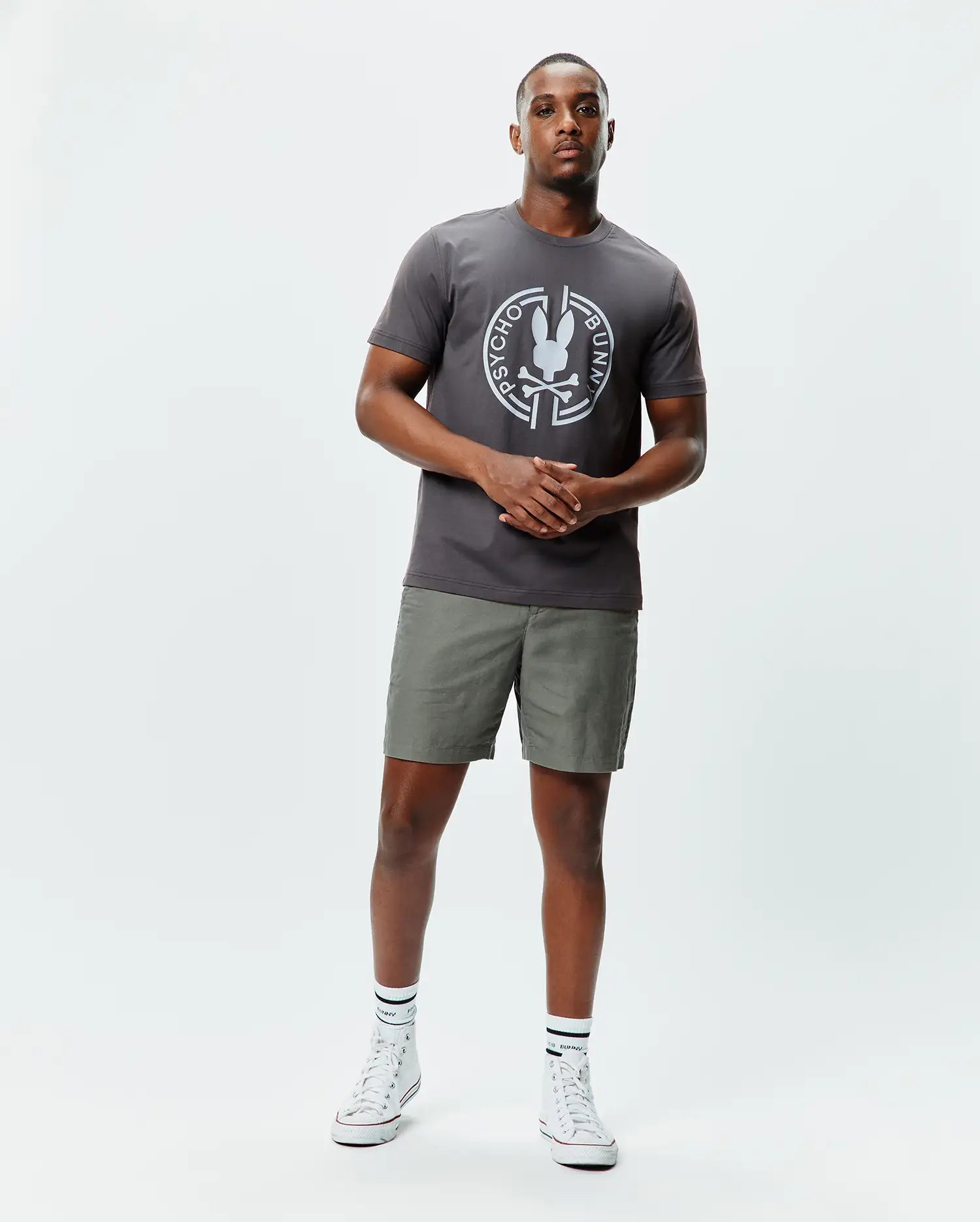 Mens Santa Fe Bunny Graphic Tee, a charcoal grey classic fit jersey t-shirt with a large white circular Psycho Bunny skull graphic on the chest, paired with olive green shorts. (4)