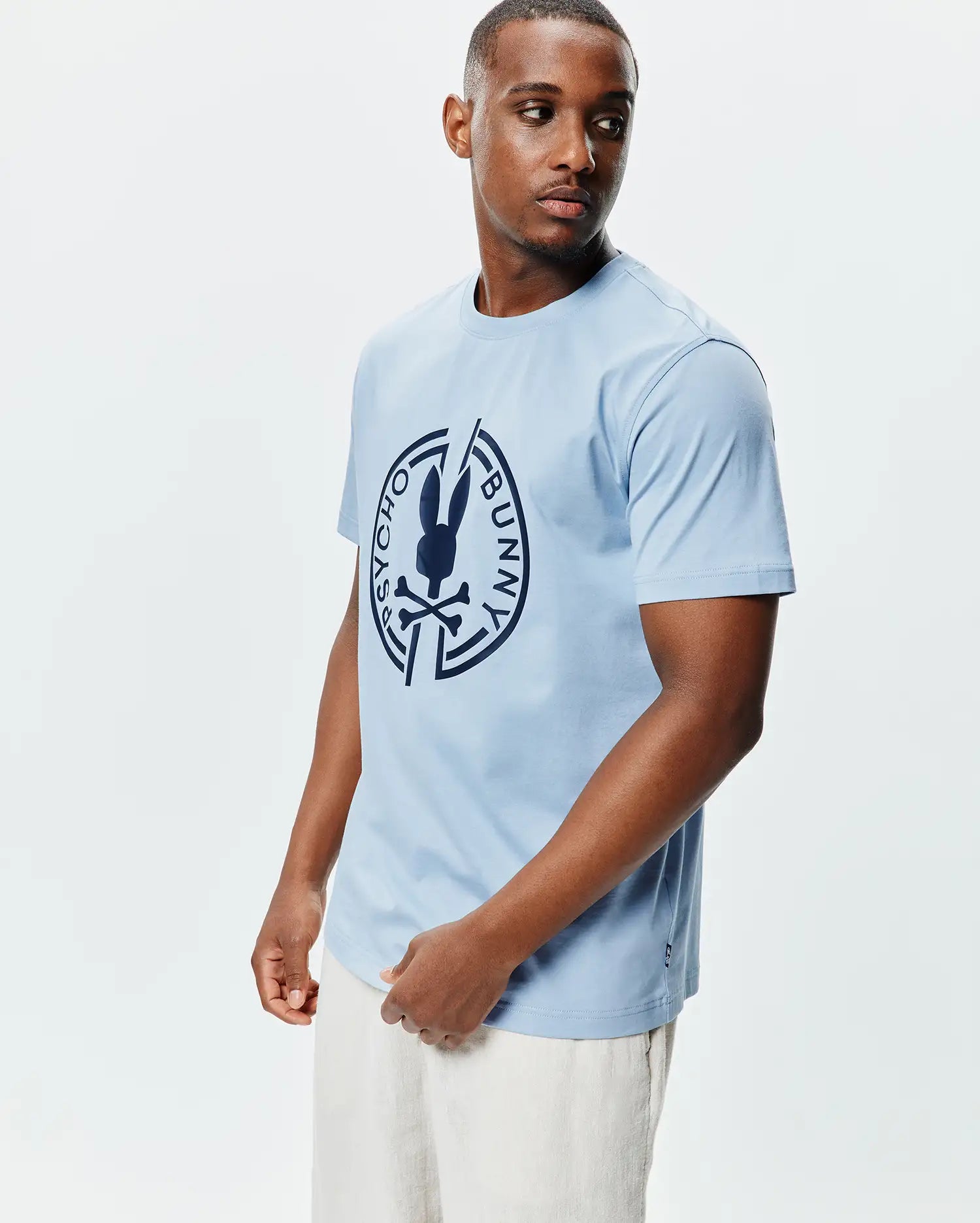 Mens Santa Fe Bunny Graphic Tee, a light blue classic fit jersey t-shirt with a large dark blue circular Psycho Bunny skull logo graphic on the chest and a small woven hem tag. (2)