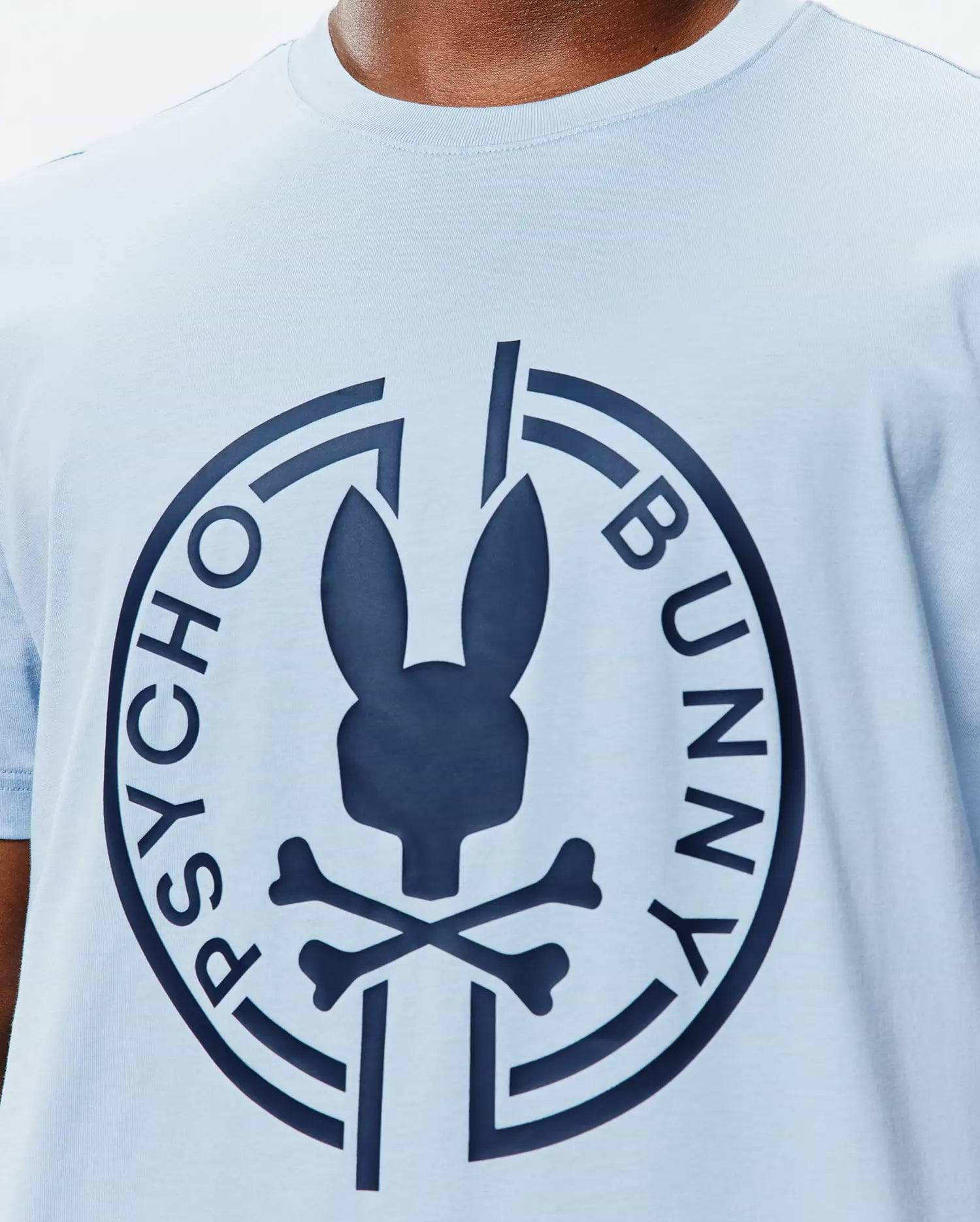Mens Santa Fe Bunny Graphic Tee, a light blue jersey knit t-shirt with a classic fit, featuring a large navy Psycho Bunny skull and crossbones logo graphic on the central chest, encircled by PSYCHO BUNNY text. (3)