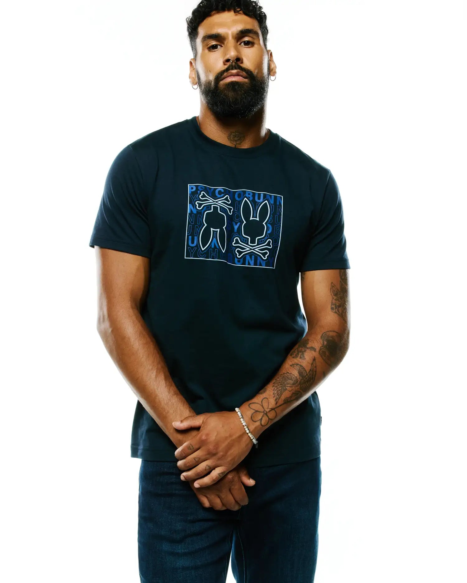 Mens Gold Coast Pima Cotton Graphic Tee, a classic fit navy blue Pima cotton jersey t-shirt featuring a large white and blue Psycho Bunny skull, crossbones, and brand text graphic on the chest.