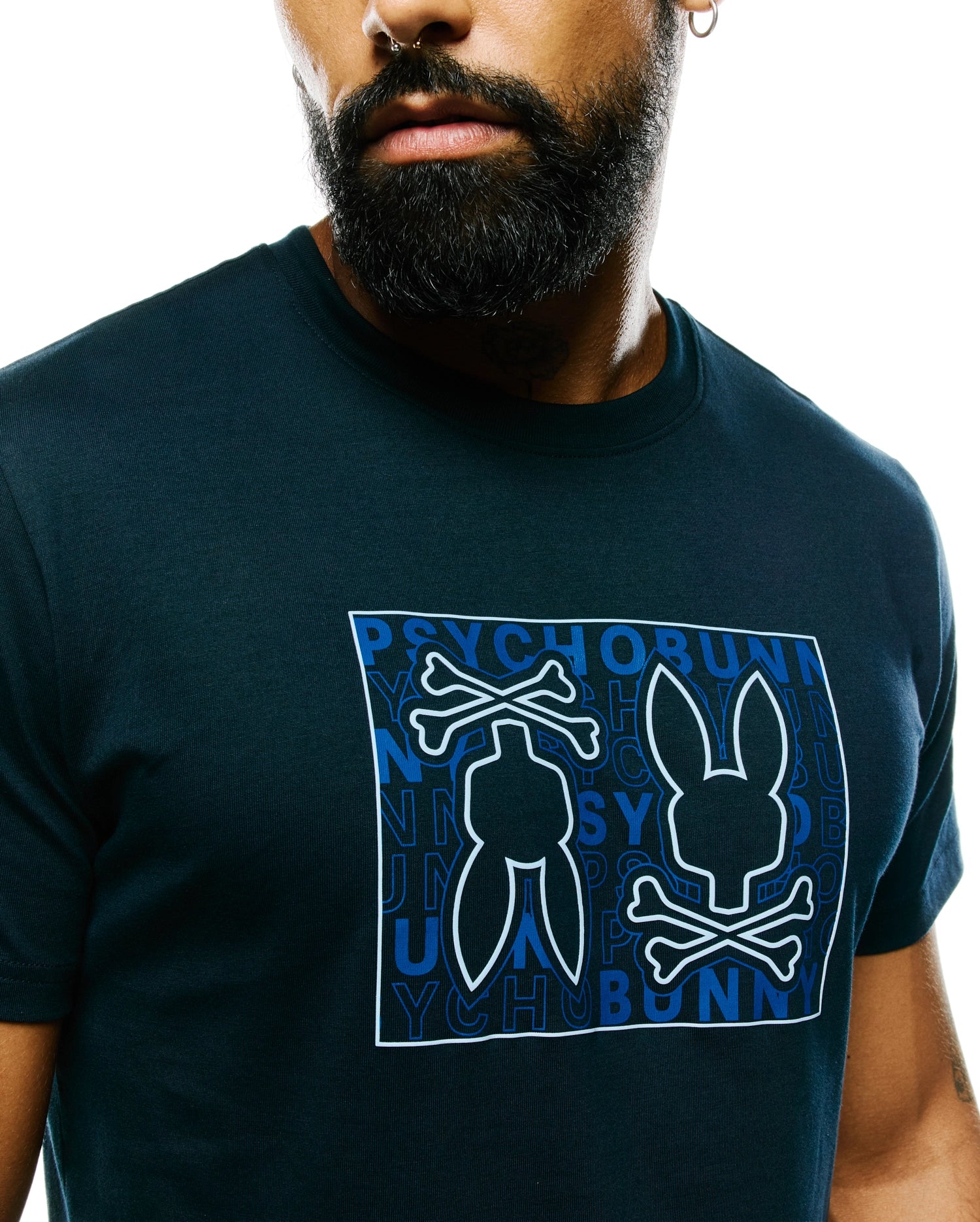 Mens Gold Coast Pima Cotton Graphic Tee: Dark navy jersey t-shirt with a large central graphic featuring the white-outlined Psycho Bunny skull logo over a blue repeated text pattern in a white rectangle, classic fit.