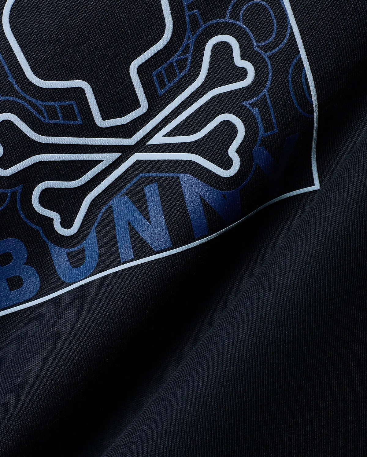 Mens Gold Coast Pima Cotton Graphic Tee in dark navy, featuring a large light blue outlined Psycho Bunny skull and crossbones logo with dark blue geometric patterns and BUNNY text on soft Pima cotton jersey.