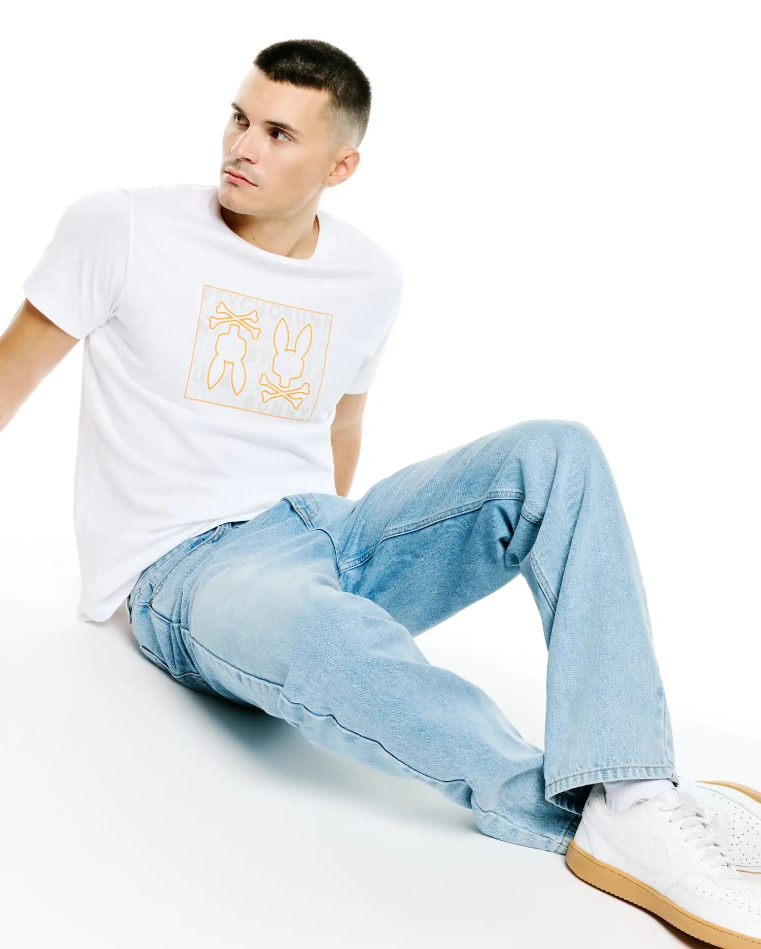 Mens Gold Coast Pima Cotton Graphic Tee, a classic fit white jersey t-shirt featuring a large orange outline chest graphic with bunny skulls, crossbones, and subtle Psycho Bunny text.