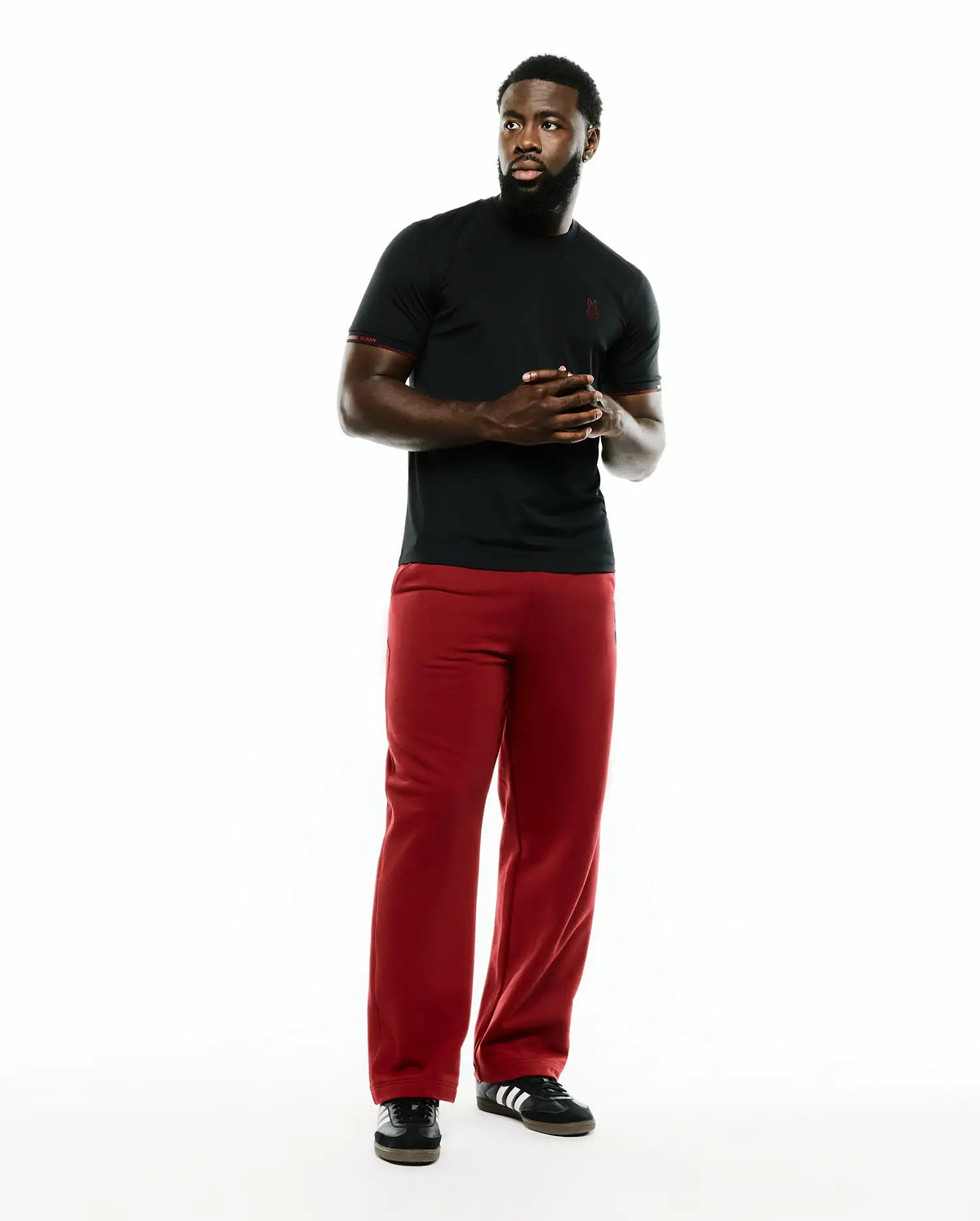 Men's Edmonds Chest Bunny Sport Tee, a black jersey t-shirt with a small red embroidered Psycho Bunny skull on the left chest and red sleeve trim, paired with relaxed fit red pants. (4)
