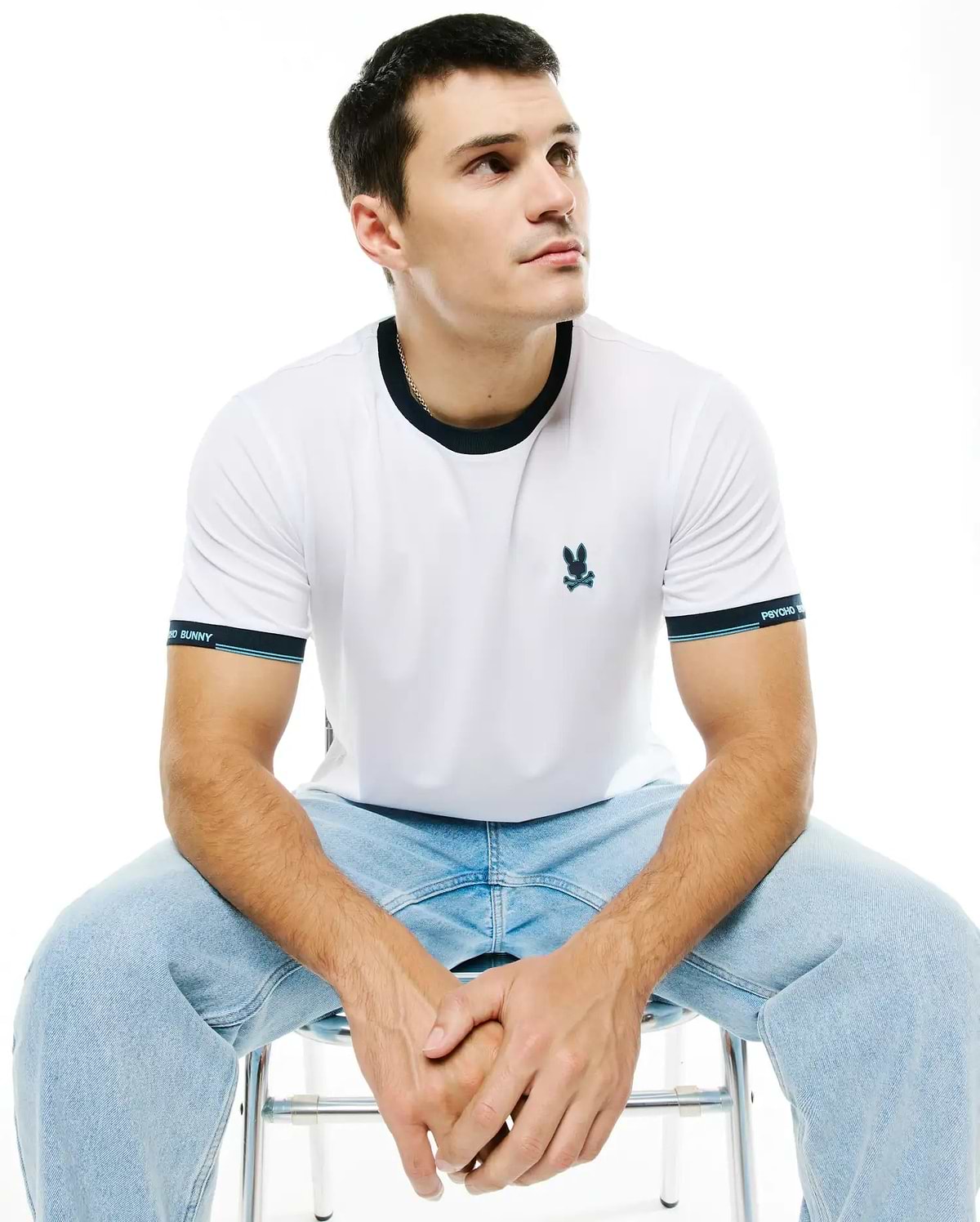 Men's Edmonds Chest Bunny Sport Tee: White jersey t-shirt with a dark blue ringer collar, banded sleeves featuring light blue stripes and Psycho Bunny text, and an embroidered teal bunny skull logo on the chest. (1)