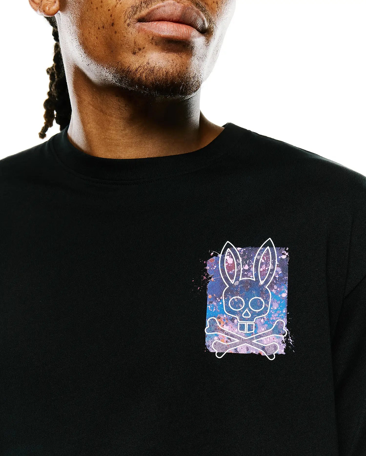 Mens Isaac Splatter Back Graphic Tee, a black jersey t-shirt with a small left chest graphic featuring a white Psycho Bunny skull and crossbones over a vibrant purple, blue, and pink splatter background.