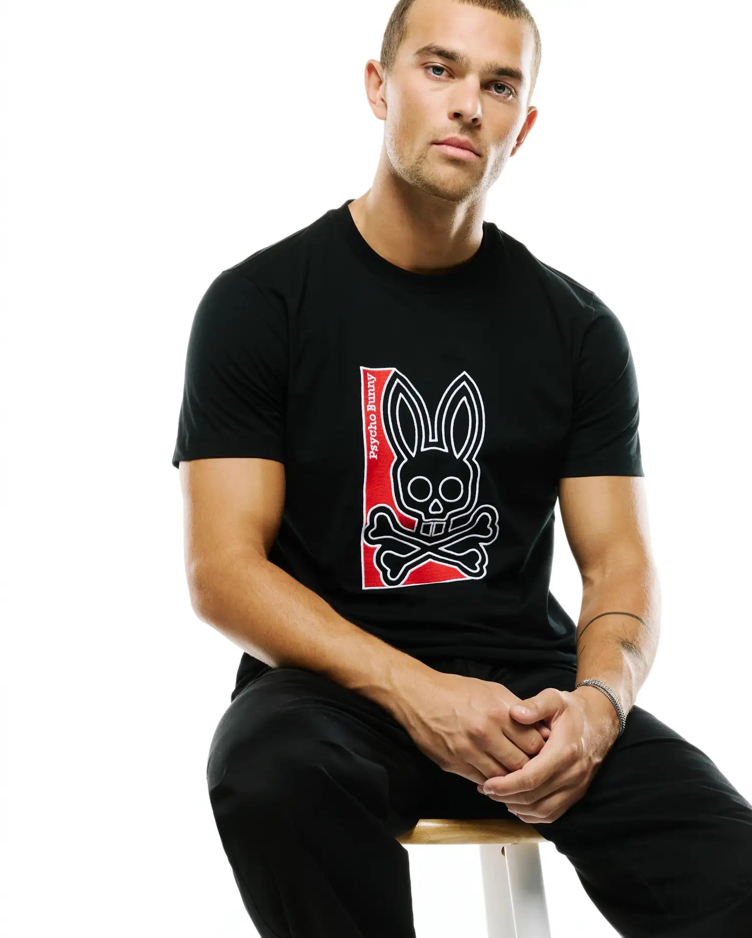 Men's Lowell Graphic Tee, a classic fit black jersey t-shirt featuring a large, centered graphic of the iconic white-outlined Psycho Bunny skull and crossbones logo on a bold red vertical panel with white Psycho Bunny text. (4)