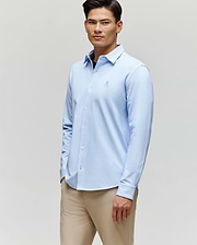 A man wearing the Psycho Bunny MENS JIM JERSEY STRIPED KNIT SHIRT (MT0300041) and beige pants stands against a plain light background, looking forward with a relaxed expression.