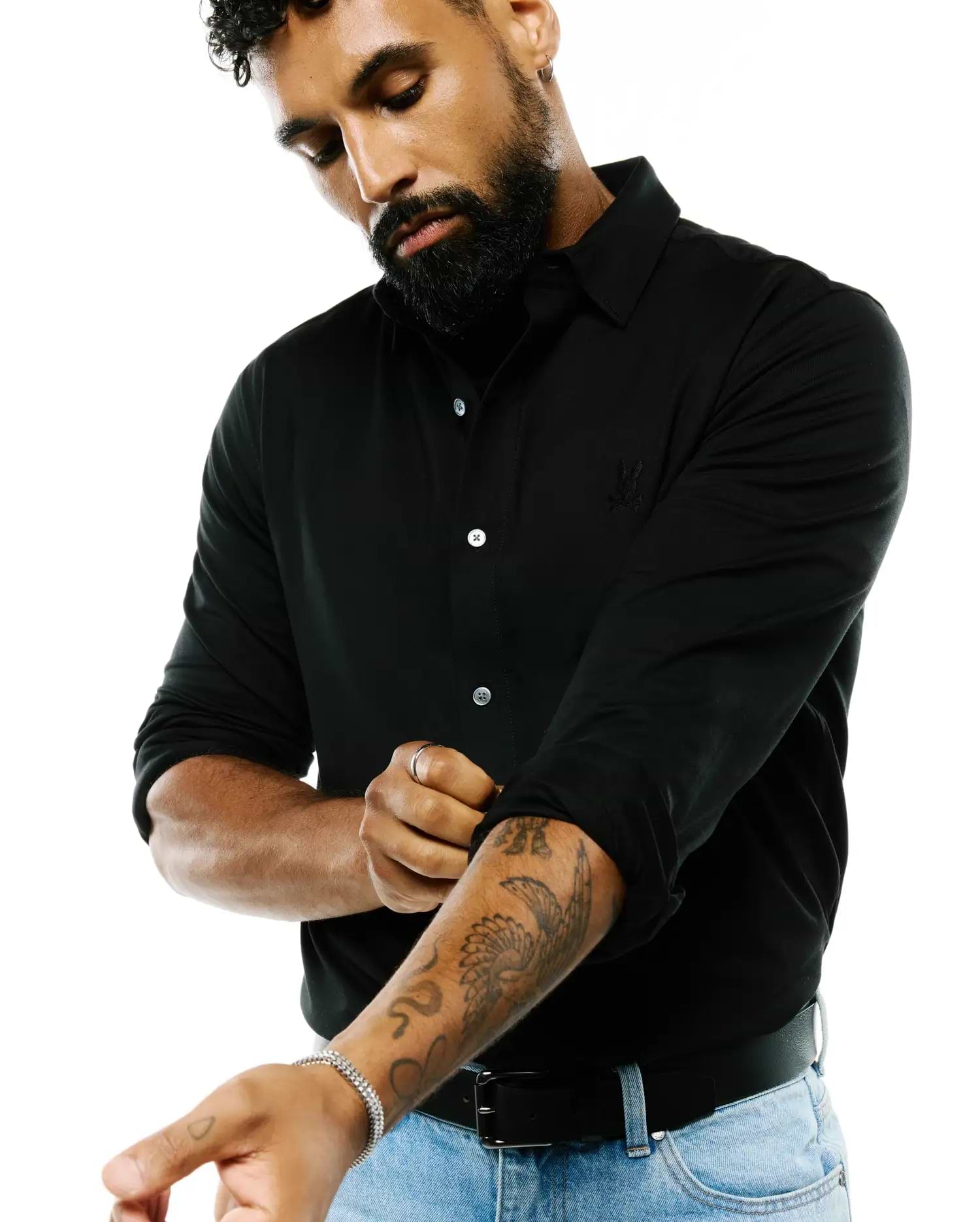 Black Mens Jim Jersey Knit Shirt, a classic fit long-sleeve with white buttons, a collared neckline, and a subtle embroidered Psycho Bunny skull logo on the left chest.