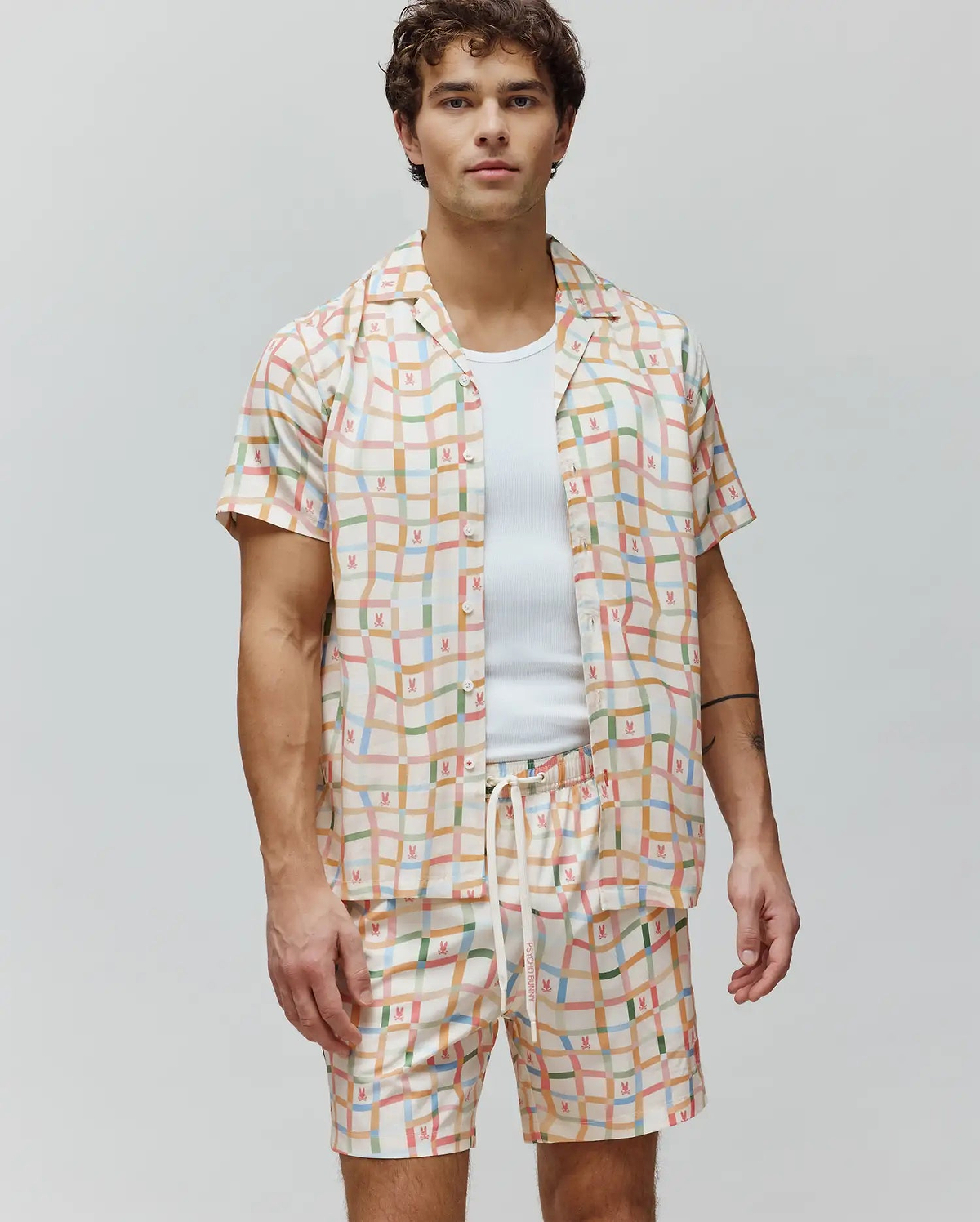 Mens Atlas Tencel Shirt, a relaxed fit cream short-sleeve button-up with a vibrant multicolor grid pattern and repeated small Psycho Bunny skull logos.