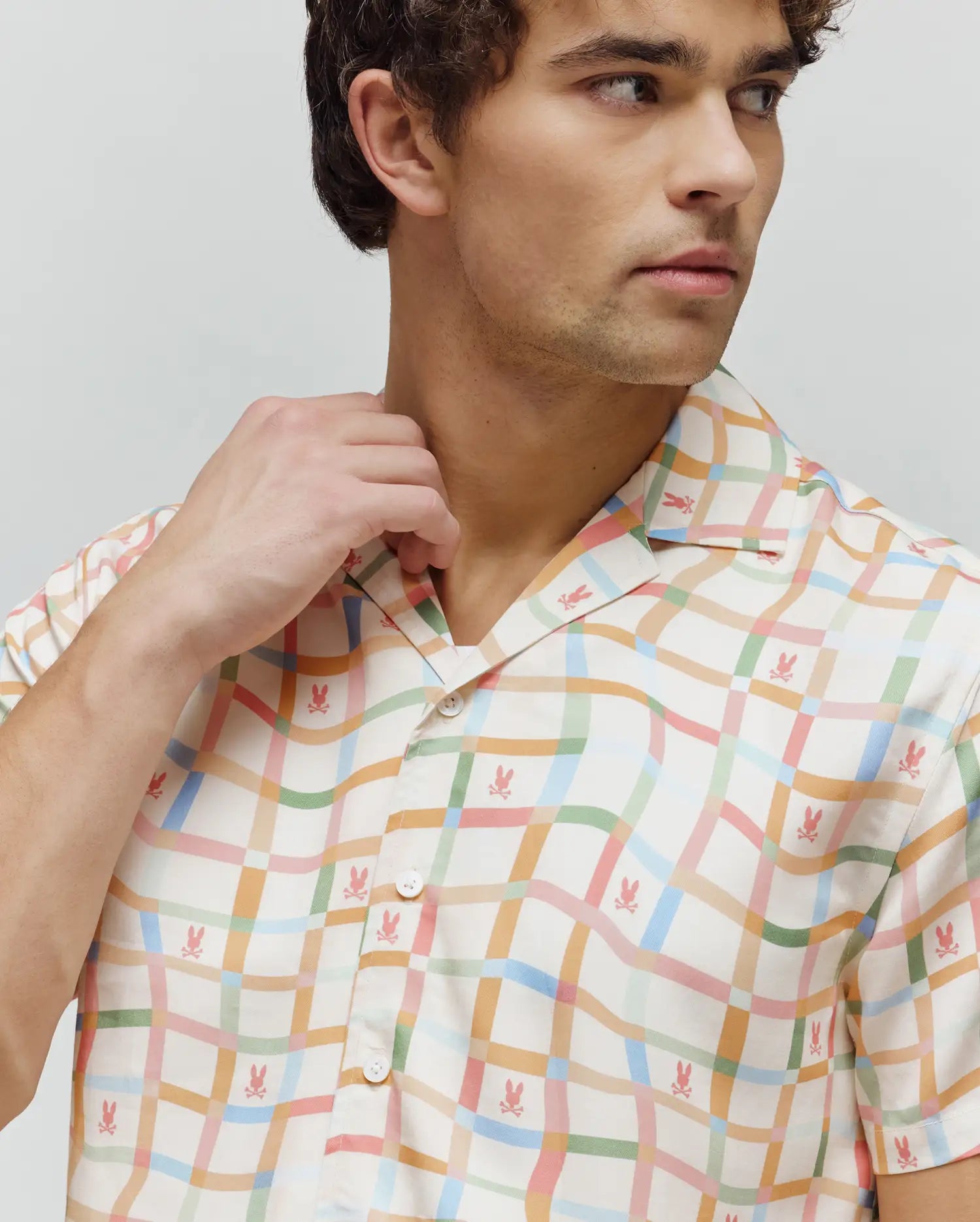 Mens Atlas Tencel Shirt, a relaxed fit, short-sleeved cream shirt with a pastel wavy plaid pattern in pink, blue, green, and orange, featuring small all-over pink Psycho Bunny skull logos.