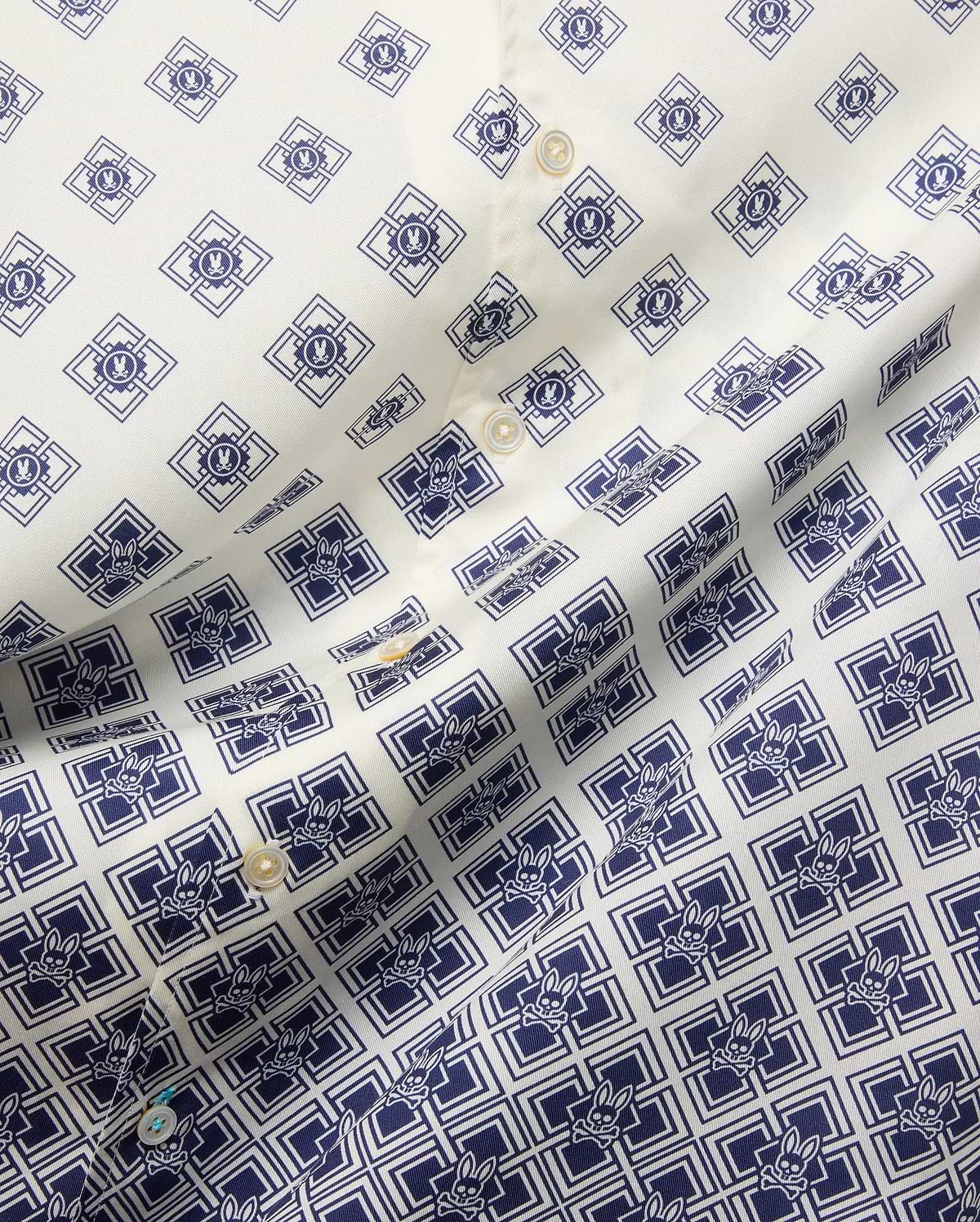Mens Tobias Tencel Shirt features an off-white smooth Tencel fabric with a repeating navy blue geometric pattern incorporating the iconic Psycho Bunny skull logo throughout, detailed with light buttons.