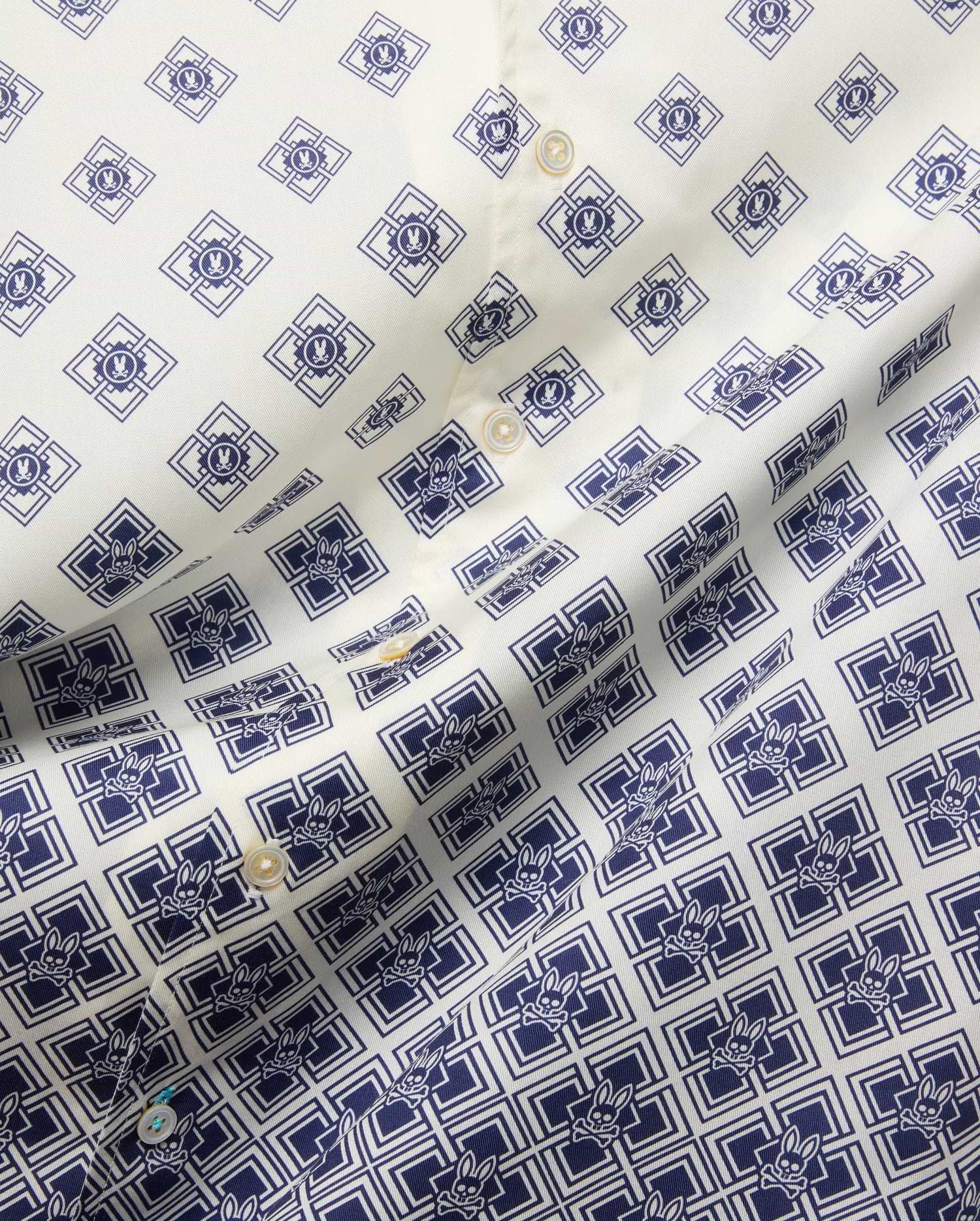 Mens Tobias Tencel Shirt features an off-white smooth Tencel fabric with a repeating navy blue geometric pattern incorporating the iconic Psycho Bunny skull logo throughout, detailed with light buttons.