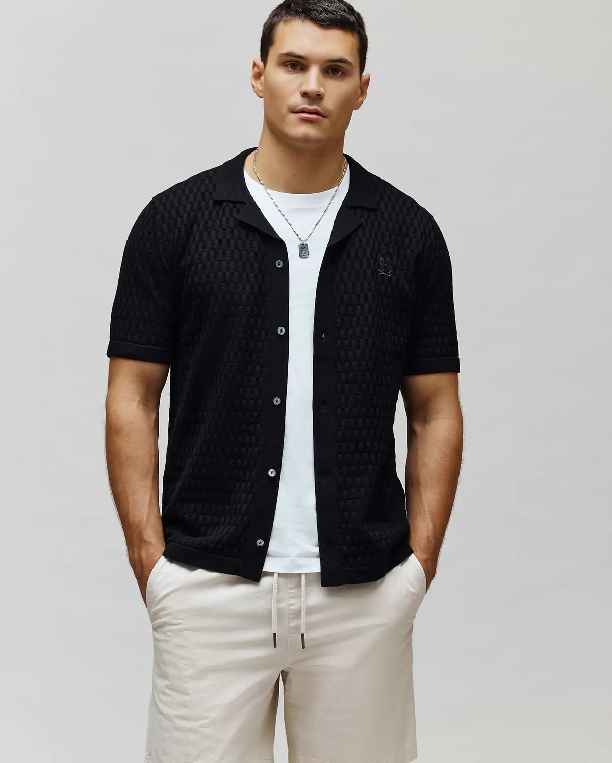 Mens Xandros Knit Shirt, black classic fit short-sleeve with a textured checkerboard knit pattern, camp collar, button-front, and small embroidered Psycho Bunny skull logo on the left chest.