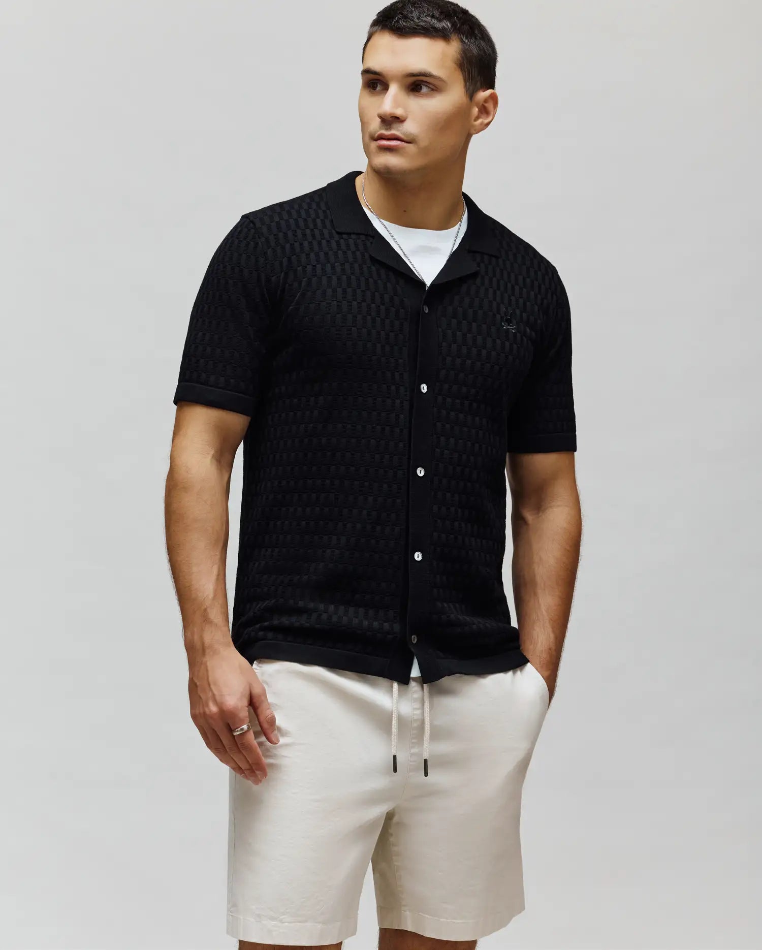 Mens Xandros Knit Shirt, black textured checkerboard knit with a classic fit, spread collar, full white button placket, and a small embroidered Psycho Bunny skull logo on the left chest.