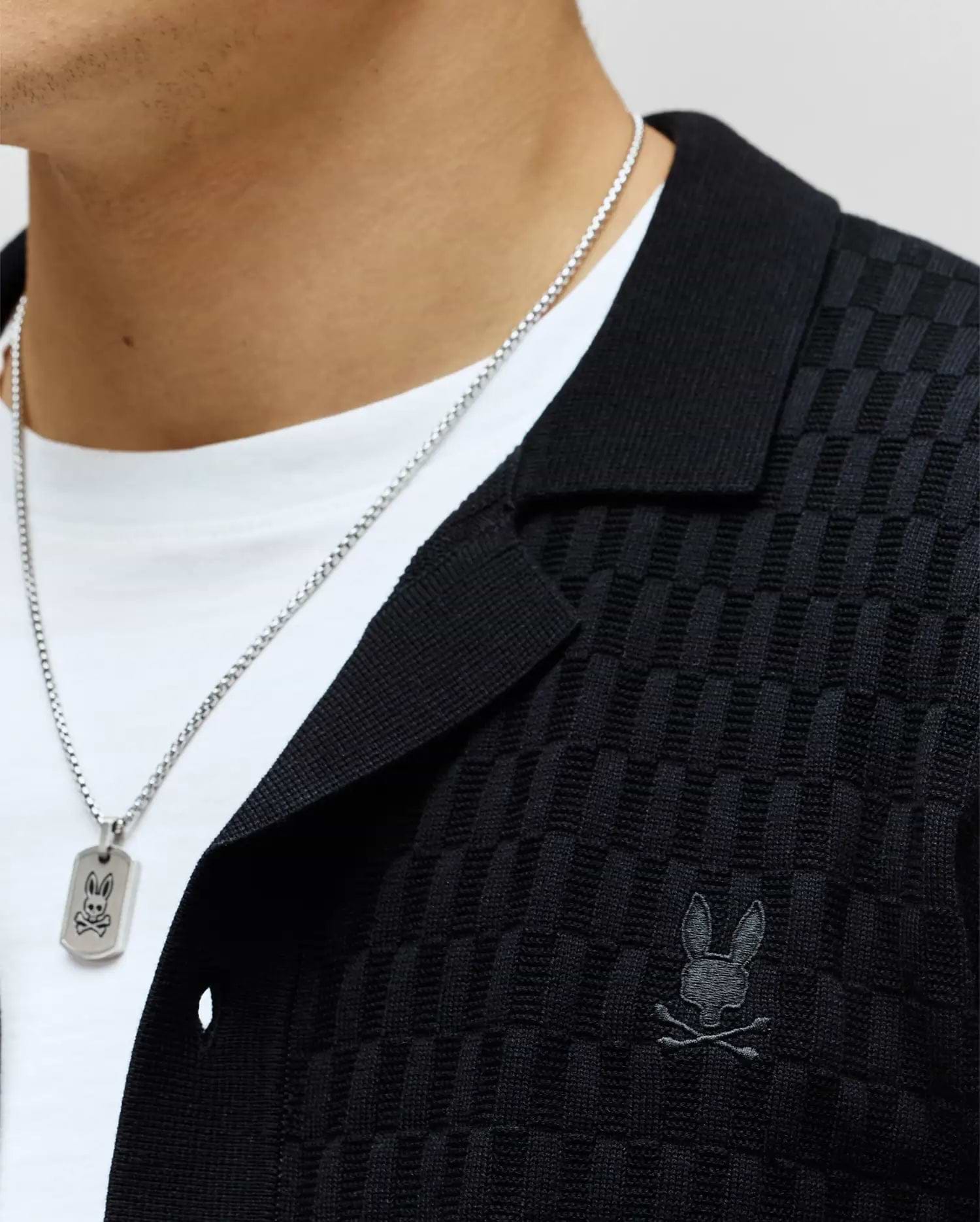 Mens Xandros Knit Shirt, black, featuring a refined checkerboard knit texture, classic collar, and a small tonal embroidered Psycho Bunny skull logo on the left chest.