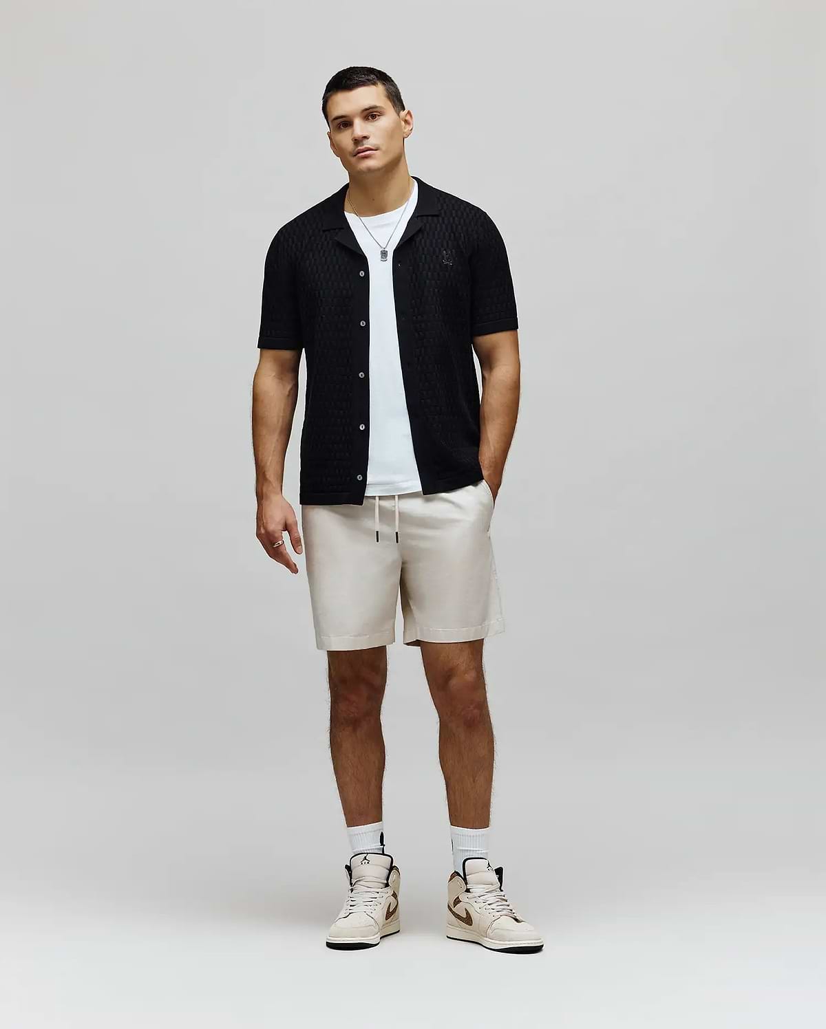 Mens Xandros Knit Shirt, a black classic fit short-sleeve knit shirt featuring a subtle geometric texture, full button-front, and a small embroidered Psycho Bunny skull logo on the left chest.