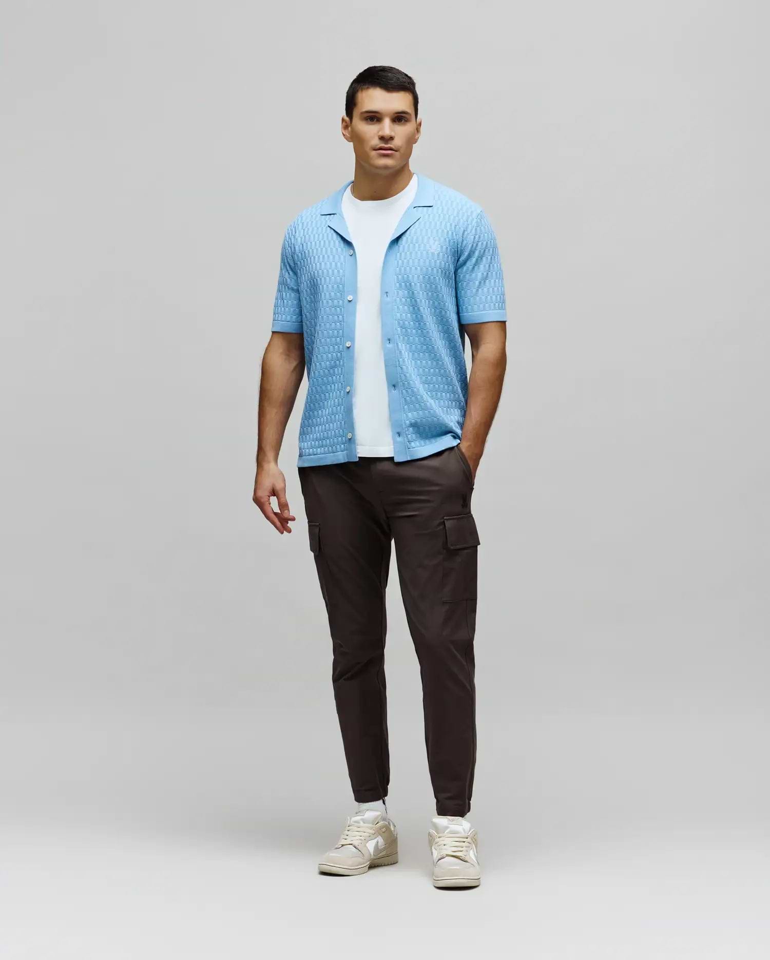 Mens Xandros Knit Shirt, a light blue relaxed-fit knit shirt with a textured woven pattern, open collar, and small embroidered Psycho Bunny skull logo on the left chest.