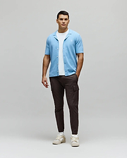 Mens Xandros Knit Shirt, a light blue relaxed-fit knit shirt with a textured woven pattern, open collar, and small embroidered Psycho Bunny skull logo on the left chest.