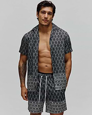 Mens Keon Tencel Shirt, a relaxed fit black short-sleeve button-up with an all-over white Psycho Bunny skull logo pattern, paired with matching shorts featuring white drawstrings. (1)