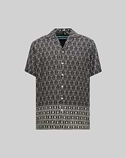 Mens Keon Tencel Shirt, black with a white all-over repeating Psycho Bunny skull logo print, featuring a relaxed camp collar and white button-front closure. (4)