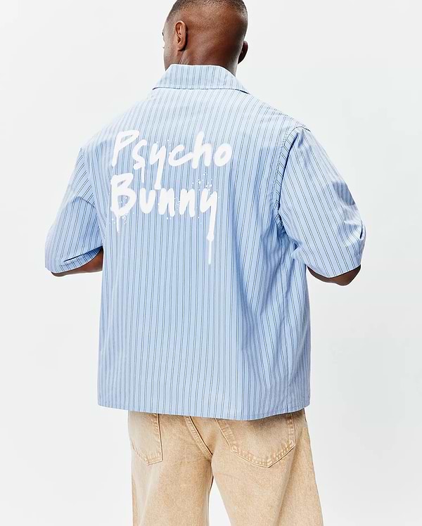 Mens Duncan Stripe Shirt: Light blue pinstripe short-sleeve shirt with a relaxed fit, smooth woven fabric, and a bold white paint-drip Psycho Bunny graphic across the upper back. (2)
