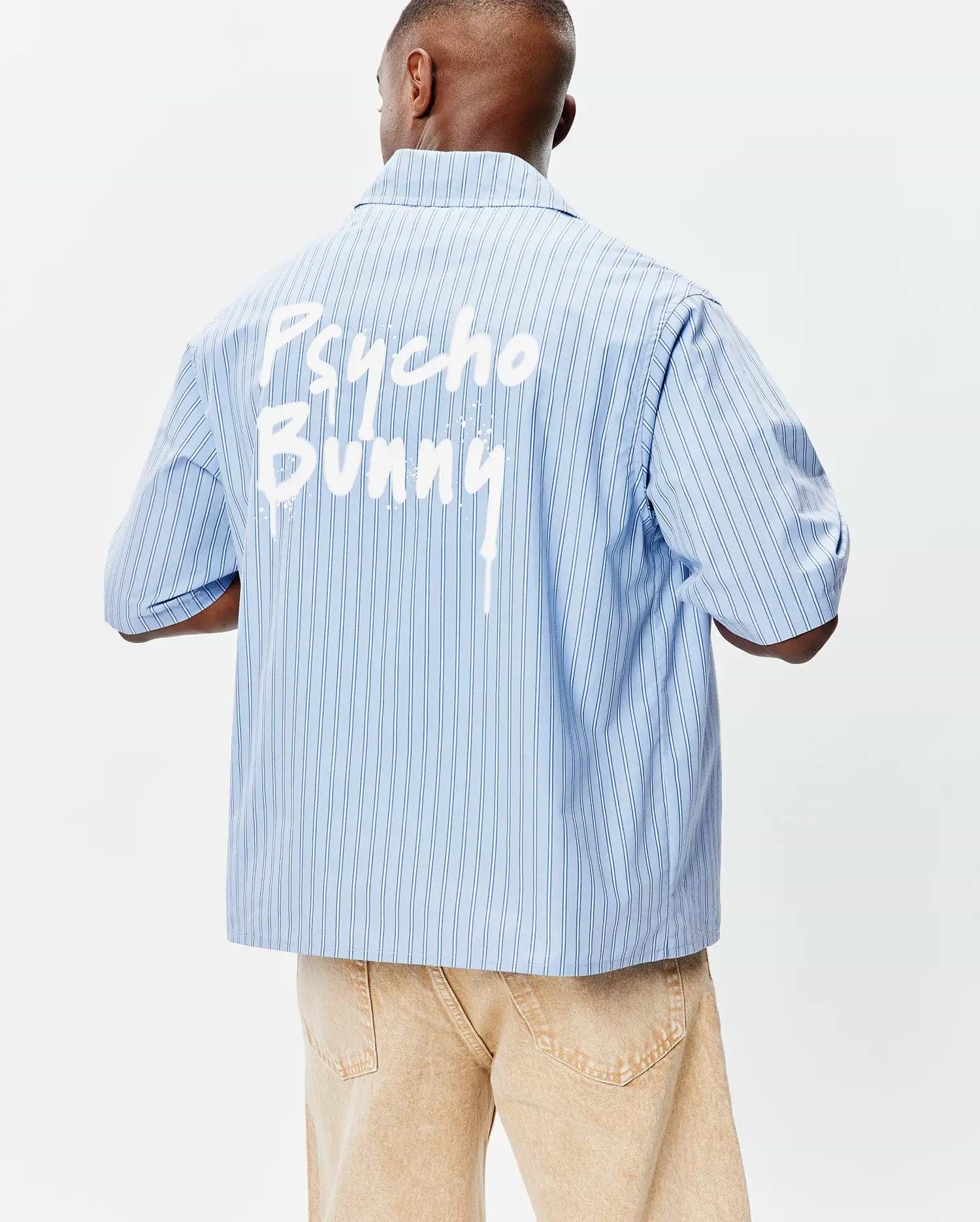 Mens Duncan Stripe Shirt: Light blue pinstripe short-sleeve shirt with a relaxed fit, smooth woven fabric, and a bold white paint-drip Psycho Bunny graphic across the upper back. (2)