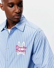 Mens Duncan Stripe Shirt, a light blue button-up with crisp dark blue and white vertical stripes. Features a large, embroidered Psycho Bunny skull logo in pink and white on the left chest, classic fit. (3)