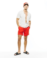 Mens Yann Knit Shirt, a white ribbed knit open-collar shirt, paired with vibrant red athletic shorts featuring a small embroidered bunny skull logo, a red Psycho Bunny cap, and black logo slides.