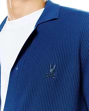 Mens Yann Knit Shirt: Deep blue ribbed knit shirt with a relaxed fit, featuring an open collar and a small, embroidered dark blue Psycho Bunny skull logo on the left chest.