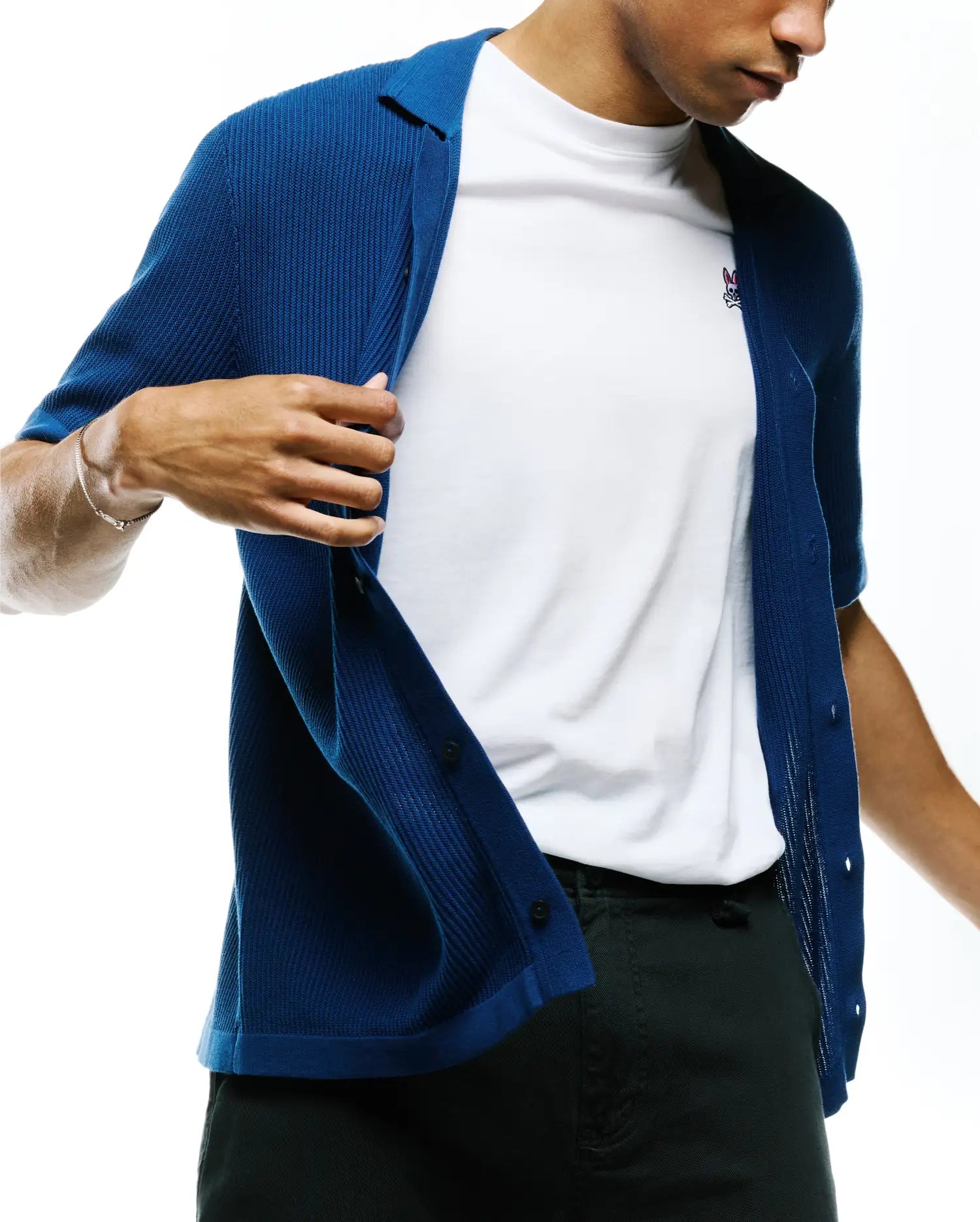 Mens Yann Knit Shirt in vibrant blue with a ribbed texture, featuring a classic collar and front buttons, layered over a white jersey t-shirt with a small, embroidered pink and white Psycho Bunny skull logo on the left chest.