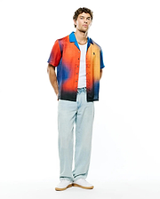 Mens Zander Jacquard Shirt, relaxed fit short-sleeve with vibrant red-orange to blue-black gradient jacquard, solid blue camp collar, and small embroidered Psycho Bunny skull logo on left chest.