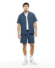 Mens Erik Raised Check Shirt and matching shorts, a relaxed navy blue set with light blue raised check stripes, featuring an open collar shirt with a small embroidered Psycho Bunny skull logo on the left chest.